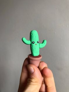 a hand holding a tiny green cactus in a clay pot with eyes on it's face