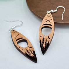 two wooden earrings with trees and birds on them sitting next to a piece of wood