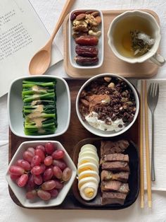 a wooden tray topped with different types of food next to utensils and a book