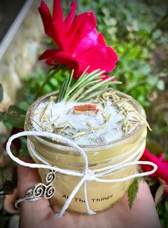 a hand holding a jar filled with some kind of drink next to a red flower