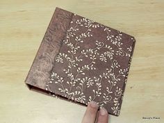 a hand is pointing at an old book with white flowers and leaves on brown paper