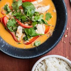 a black bowl filled with soup and garnished with cilantro, red peppers, and green leaves