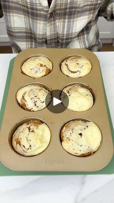 a person holding a muffin pan with six muffins in it on a counter