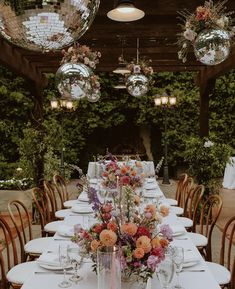 a long table is set with flowers and wine glasses in front of mirrored disco balls hanging from the ceiling