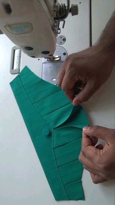 two hands are working on a green piece of paper that is being sewn together