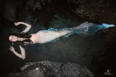 a woman in a mermaid costume floating on top of a body of water next to rocks