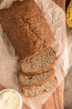 sliced loaf of banana bread sitting on top of a piece of wax paper next to a bowl of butter