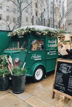 a green food truck parked in front of a building with christmas decorations on the roof