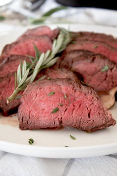 some meat is on a white plate and garnished with fresh herbs, ready to be eaten