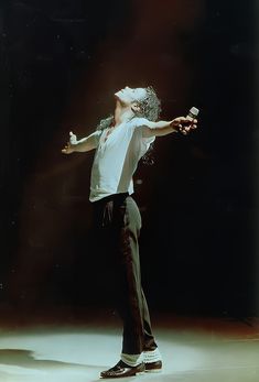 a man in white shirt and black pants standing on stage with his arms spread out