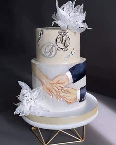 a three tiered wedding cake with two hands holding each other's fingers on a plate