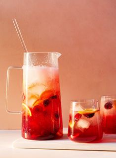 three glasses and pitcher filled with liquid sitting on a table