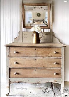 an old dresser with a mirror and vase on it's top, in front of a white wall