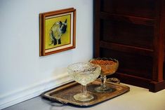 two wine glasses are sitting on a tray in front of a framed animal print and artwork