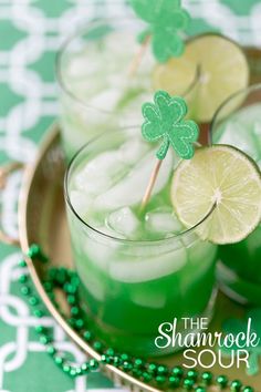 two glasses filled with green liquid and lime slices on top of each other, sitting on a plate