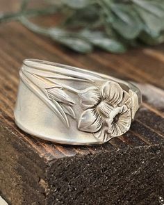 a silver flower ring sitting on top of a wooden table next to a leafy plant