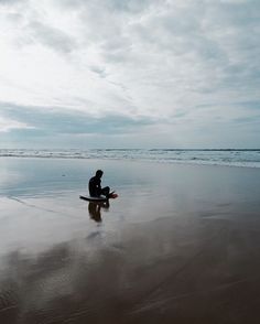 a man sitting on top of a surfboard in the sand at the ocean's edge