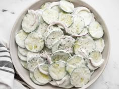 a white bowl filled with cucumbers and dill on top of a table