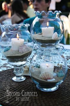 two clear vases filled with sand and lit candles on top of a table cloth