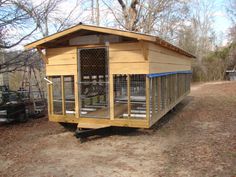 a chicken coop in the middle of a dirt field with trees and bushes behind it