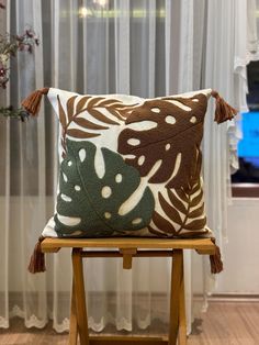 a decorative pillow sitting on top of a wooden chair in front of a white curtain