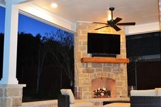 an outdoor fireplace with a tv mounted on it's side and a ceiling fan