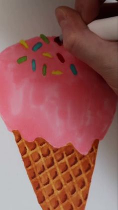 a hand holding an ice cream cone with pink frosting and sprinkles