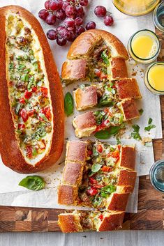 bread filled with meat and vegetables on top of a cutting board next to glasses of orange juice