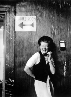 an old black and white photo of a woman talking on the phone while standing in front of a door