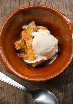 a brown bowl filled with food on top of a wooden table next to a spoon