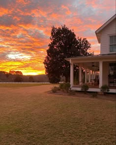 the sun sets over a large house with porches and chairs on the front lawn