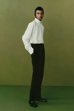 a man standing in front of a green background wearing a white shirt and black pants