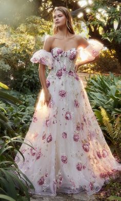 a woman in a white and pink dress standing on a stone path surrounded by greenery