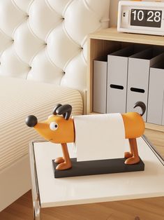 an orange dog figurine on a white table in front of a bed and storage bins