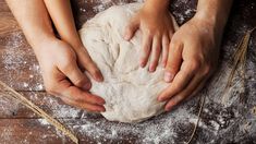 two hands on top of a ball of dough with wheat stalks around it and flour in the background