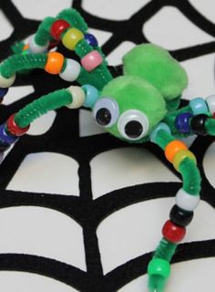 a green spider made out of beads on a black and white tablecloth with webs