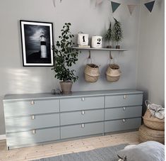 a bedroom with grey dressers and plants on the shelf above them, along with two baskets