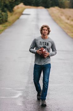 a man is walking down the street with a football in his hand and wearing a titan t - shirt