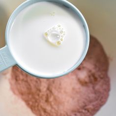 a cup filled with milk sitting on top of a white table next to a pile of dirt