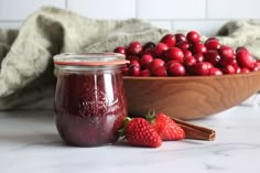 a bowl of cranberry sauce next to a wooden bowl filled with strawberries