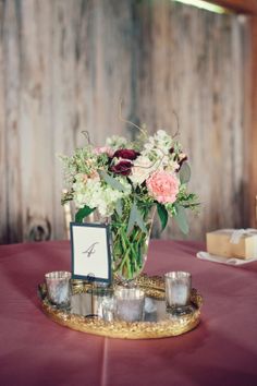 a vase with flowers and candles on a table in front of a wooden wall at a wedding reception