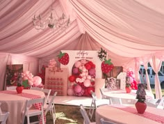 a pink and white tent with tables, chairs, and balloons on it's walls