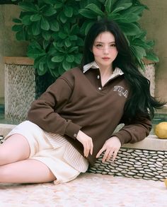 a woman sitting on the ground next to a potted plant wearing a brown sweater and white skirt