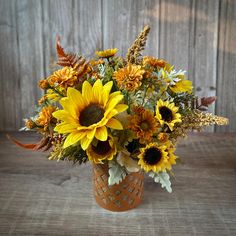 a vase filled with sunflowers and other flowers on top of a wooden table