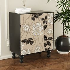 a black and white cabinet sitting next to a plant on top of a hard wood floor