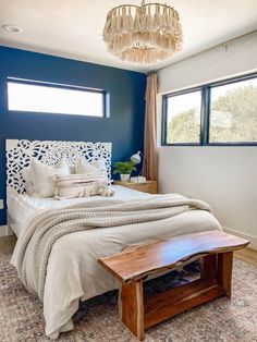 a bedroom with blue walls, white bedding and a wooden bench in the middle