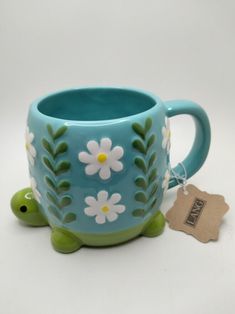 a blue mug with white daisies on it and a tag attached to the handle