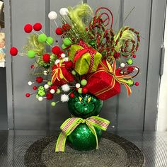 a green vase filled with lots of red and green flowers on top of a table