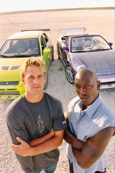 two men standing next to each other in front of cars