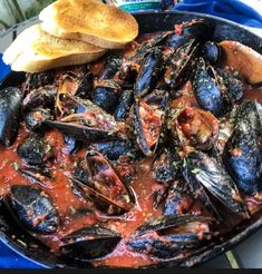 a pan filled with mussels and sauce next to bread